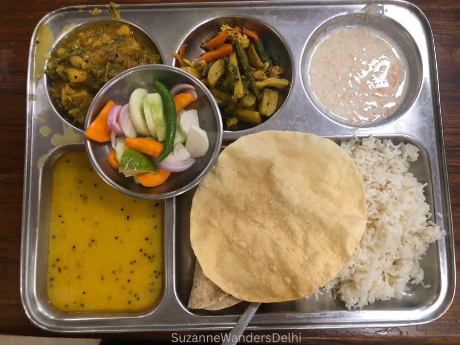 rectangular metal thali tray with different vegetable dishes, dal, raita, rice, pappadam and rotis