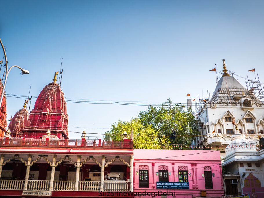red spires of Sri Digambar Jain Lal Mandir on the left and white tower of Shri Guari Temple on the right with blue sky on Chandni Chowk